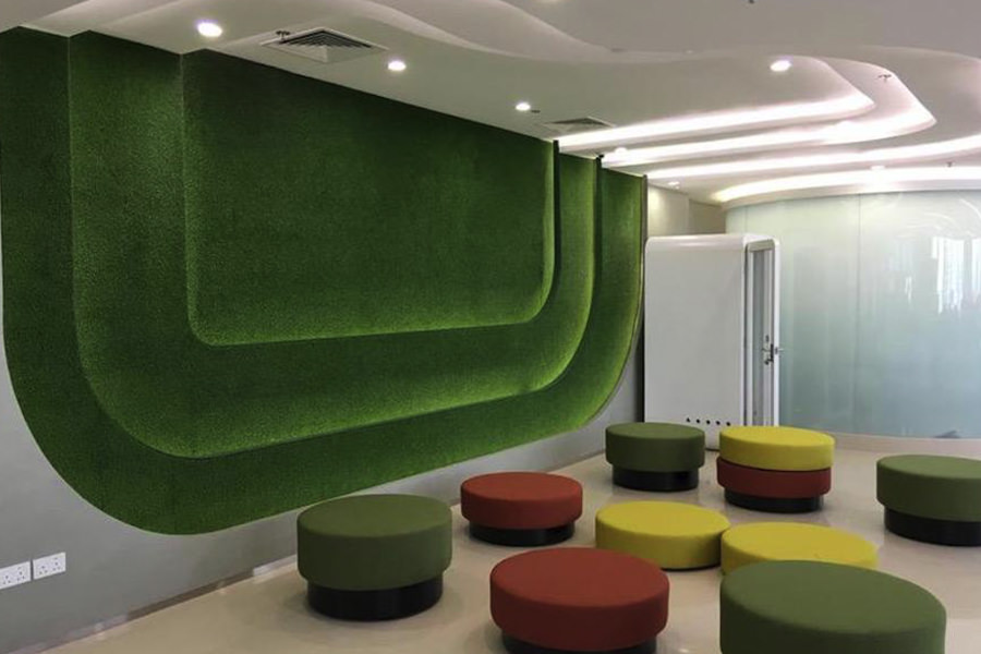 Creative office lounge featuring a green moss wall and colorful ottoman seating by Almoayyed Contracting Group.